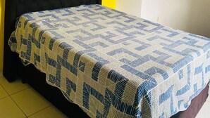 Un lit avec une couvre-lit à motifs, une tête de lit noire recouverte de tissu et deux décorations murales en forme de cœur.