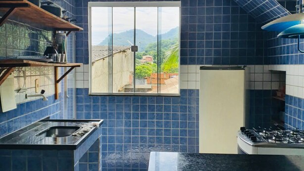 Une cuisine avec des carreaux bleus, une fenêtre donnant sur un beau paysage, une cuisinière à gaz et un évier.