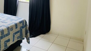 Une chambre avec un lit, une fenêtre avec des rideaux, un appareil de climatisation et un revêtement de sol carrelé.