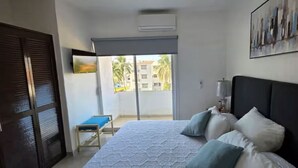 A bedroom with a bed, a small table, a chair, a balcony with a view of buildings, and a painting on the wall. - Entire Condo in a Gated Community with Spectacular Views  in Manzanillo, Mexico (Manzanillo)