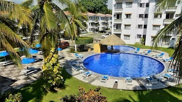 A hotel with a circular pool surrounded by lounge chairs and palm trees. - Entire Condo in a Gated Community with Spectacular Views  in Manzanillo, Mexico (Manzanillo)