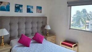 A bedroom with a large bed, bedside lamps, a nightstand, a window with a view, and wall-mounted air conditioning. - Entire Condo in a Gated Community with Spectacular Views  in Manzanillo, Mexico (Manzanillo)