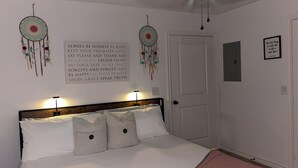 Ett sovrum med en säng, två väggdekorationer, en dörr och ett inramat citat på väggen.