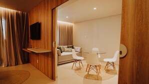 A modern room with a wooden accent wall, a flat-screen TV, a sofa, a dining table with chairs, and a small rug. - POUSADA BOSQUE DA SERRA (Crato)