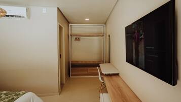 Una habitación de hotel con cama, escritorio, televisor, armario y un banco.