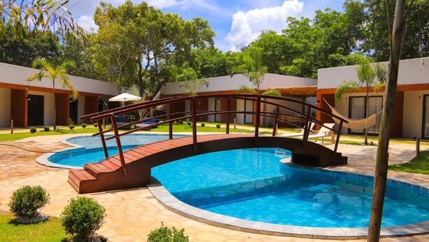 A swimming pool with a wooden bridge, surrounded by buildings with a consistent architectural style. - POUSADA BOSQUE DA SERRA (Crato)
