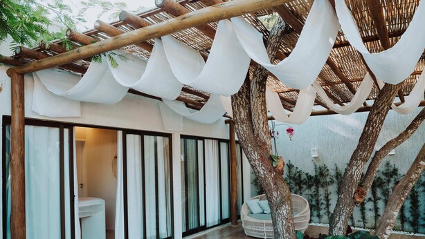 Une terrasse extérieure moderne, dotée d’une pergola en bois, d’un fauteuil suspendu et d’un petit espace jardin avec des plantes.