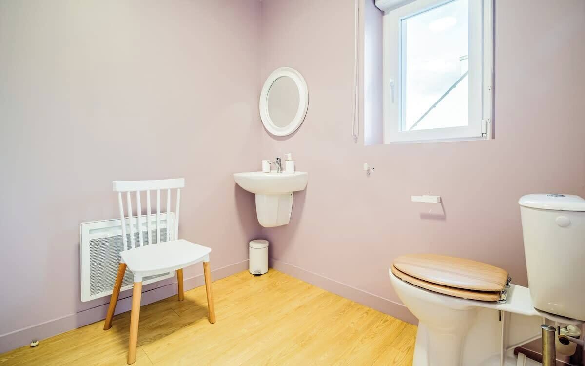 A small bathroom with a white sink, a toilet, a white chair, and a radiator.