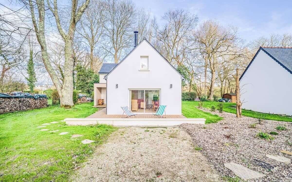 Une maison moderne dotée d’une grande porte vitrée, d’un petit balcon et d’un jardin avec un chemin de gravier.