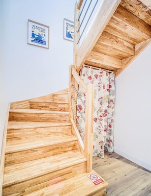 Un escalier en bois avec des rampes en métal, un rideau à motifs floraux et deux affiches encadrées accrochées au mur.