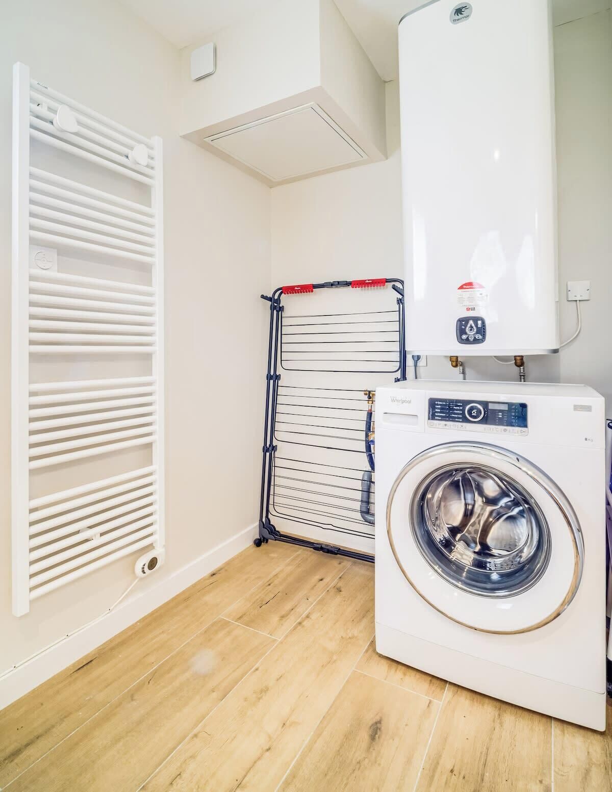 A laundry room with a white washing machine, a drying rack, and a vented heater.