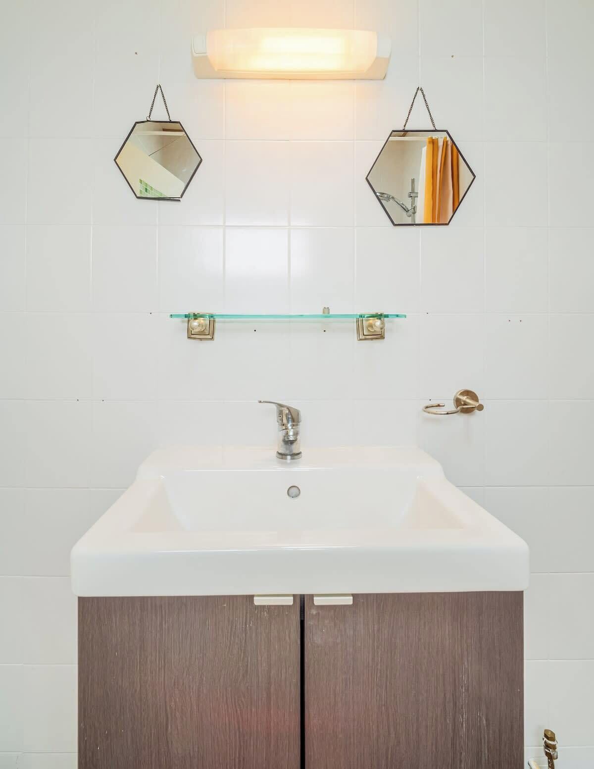 Ein Badezimmer mit einem weißen Waschbecken, zwei sechseckigen Spiegeln, einer Glasablage und einem Holzkorpus.