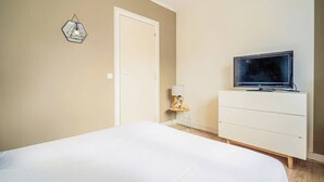 Un dormitorio con cama, televisor en una cómoda, una puerta y una lámpara fijada a la pared.