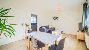 Un espacio habitable compacto con una mesa de comedor, sillas, un sofá, un televisor y una planta.