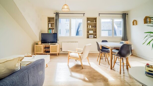 Una sala de estar moderna con un sofá, una mesa de comedor, sillas, un televisor y estanterías empotradas.