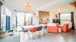Una sala de estar moderna con comedor, un conjunto de sofá, televisor y un amplio ventanal con cortinas.