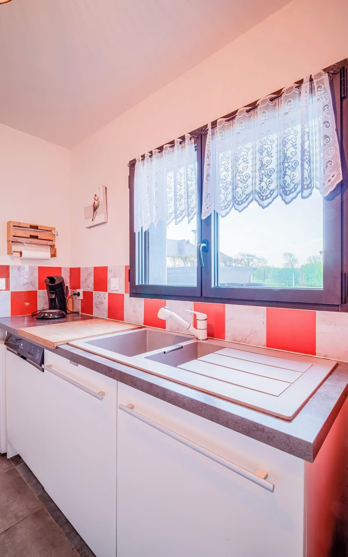 Cucina con lavello doppio, macchina da caffè e finestra con tende in pizzo.