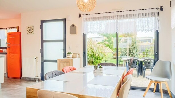 Una cocina moderna con un refrigerador rojo, un comedor con una mesa grande y sillas, y vistas a zonas verdes al exterior.