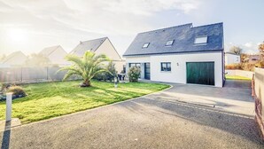 Una casa moderna de dos pisos con techo inclinado, puerta verde y un pequeño jardín con una palmera.