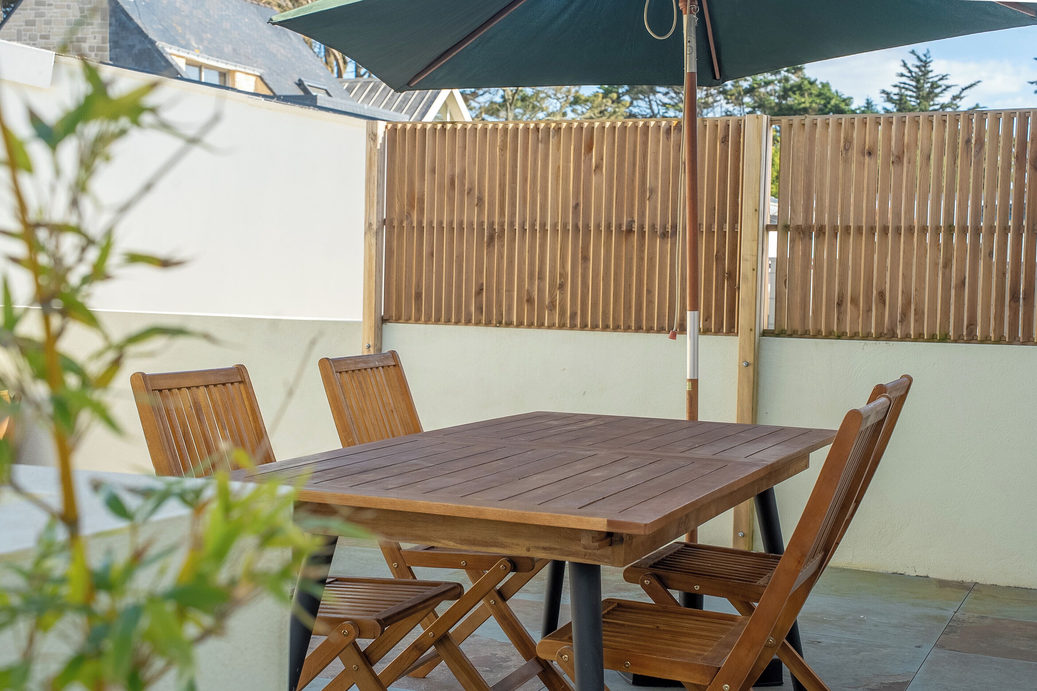 Un patio al aire libre con una mesa y sillas de madera, una cerca de madera y un paraguas verde.