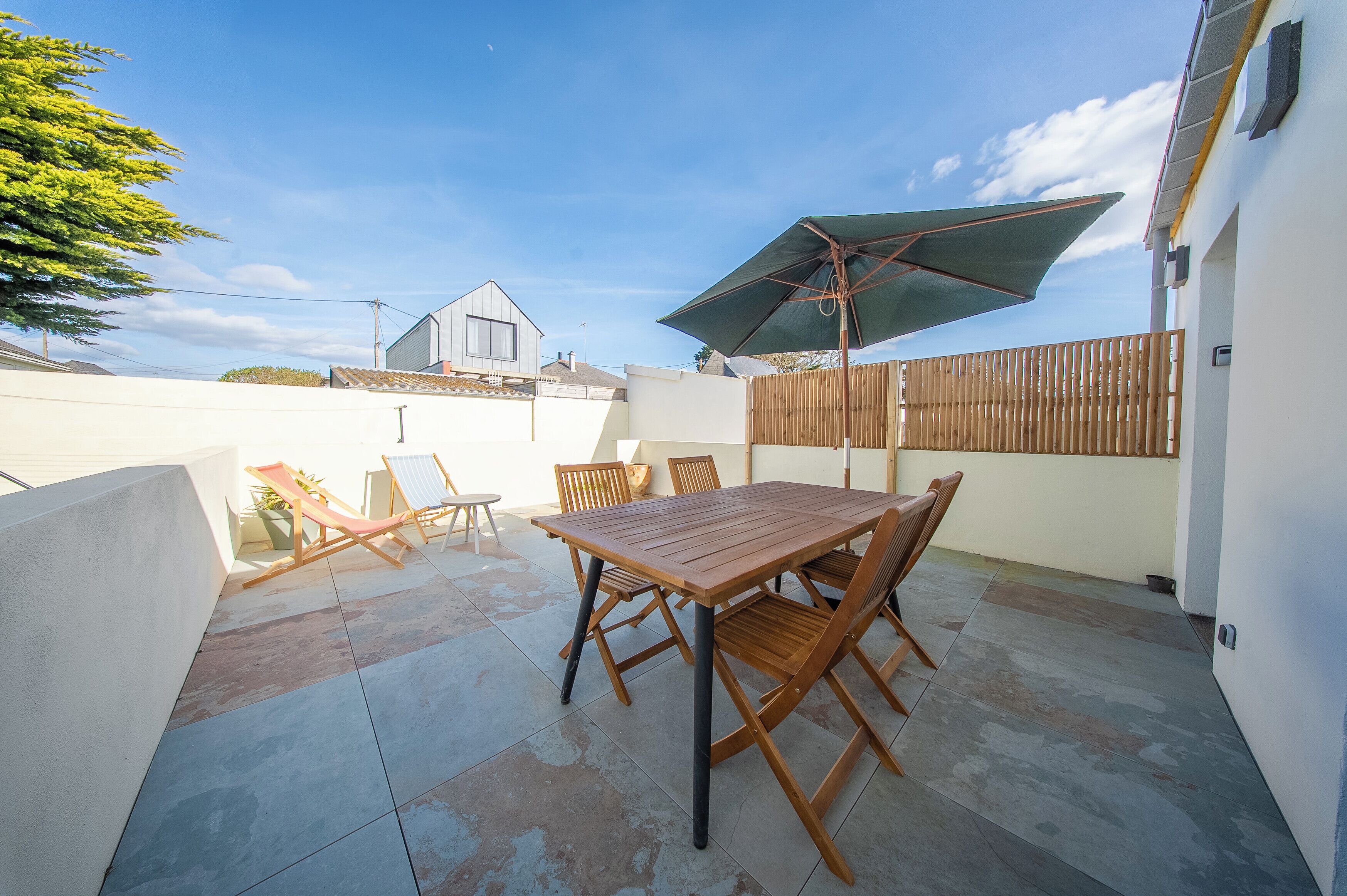 A patio with a wooden table and chairs, a folding chair, and a large umbrella.