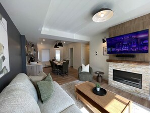 A modern living room with a sofa, coffee table, fireplace, and TV. - Brookside Peaks | Downtown | Rooftop Hot Tub (Canmore)