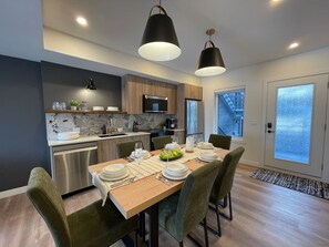 A modern kitchen with a dining area, stainless steel appliances, and a large window. - Brookside Peaks | Downtown | Rooftop Hot Tub (Canmore)