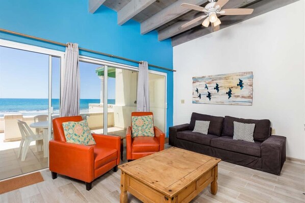A room with a large window overlooking the ocean, a ceiling fan, a wooden coffee table, and two sofas. - Las Olas II 2 | 3BR Beachfront Condo | Sleeps 7 (Puerto Peñasco)