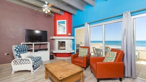 Ein Wohnzimmer mit Fernseher, Kamin, Deckenventilator und Blick auf den Strand.