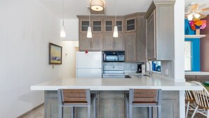 Eine Küche mit Holzausstattung, einer weißen Kücheninsel mit Barhocker, einer Mikrowelle und einem Kühlschrank.