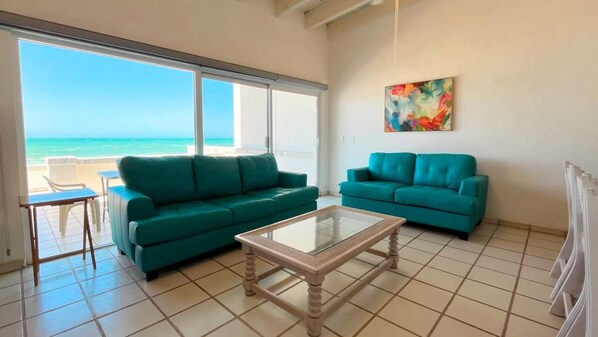 Une pièce avec deux canapés de couleur turquoise, une table basse en verre et une vue sur l’océan.