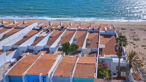 Un hotel costero con techos de tejas de barro, paredes blancas y vista a la playa.