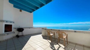 Un balcón con una parrilla, dos sillas y vista al mar.