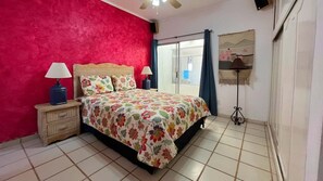 Une chambre à coucher comprenant un lit, deux lampes de chevet, une table de chevet, une fenêtre avec des rideaux et une lampe fixée au mur.