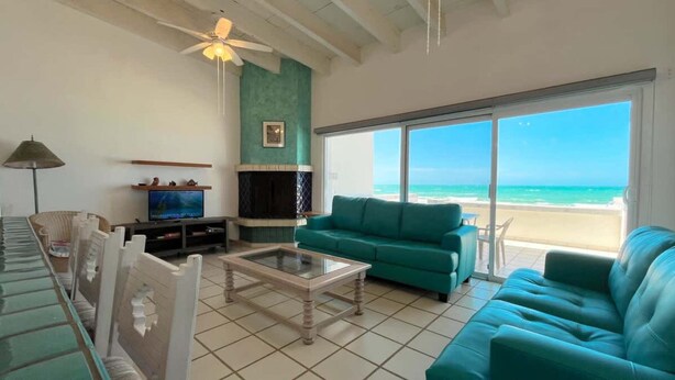 Una sala de estar con televisión, chimenea, sofá y vista a la playa.