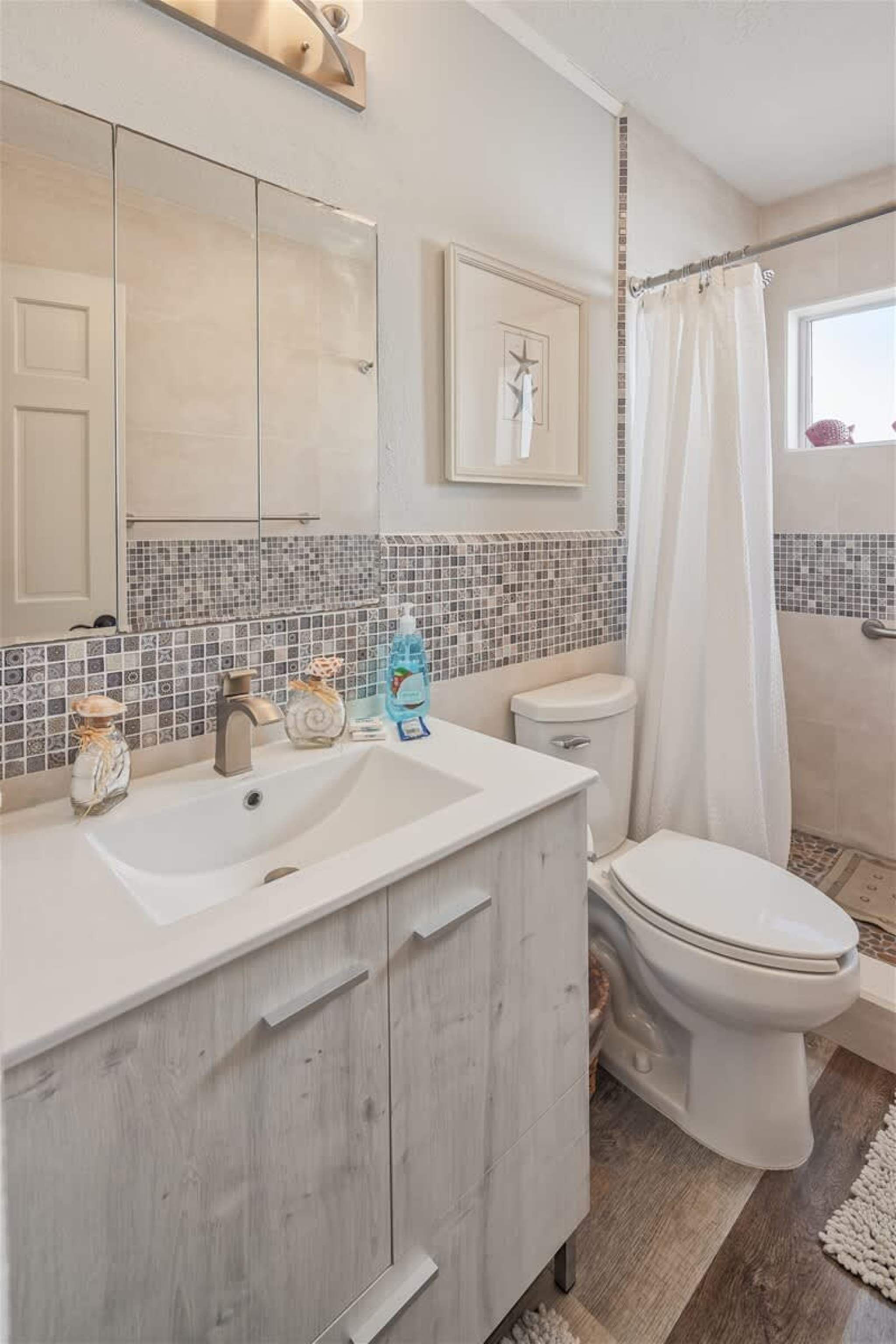 Un baño con lavamanos blanco, inodoro, ducha con cortina y salpicadero de azulejos.