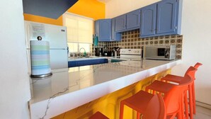 Une cuisine moderne avec des meubles bleus, un plan de travail blanc et des tabourets de bar orange.