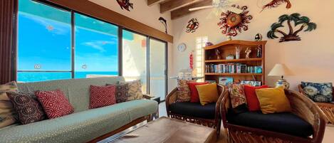 Een woonkamer met een bank, fauteuils, een boekenkast en uitzicht op zee.