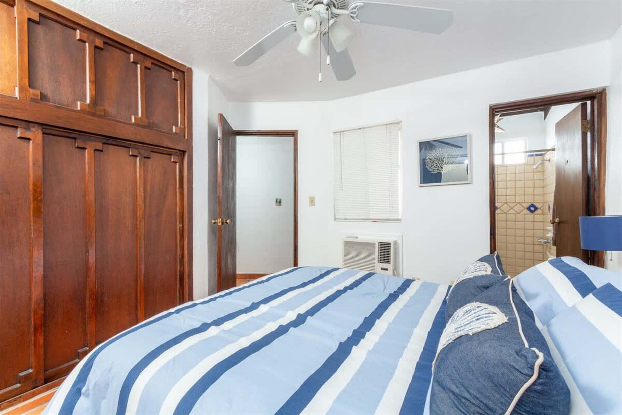 A bedroom with a bed, a ceiling fan, a wooden wardrobe, and a bathroom door.