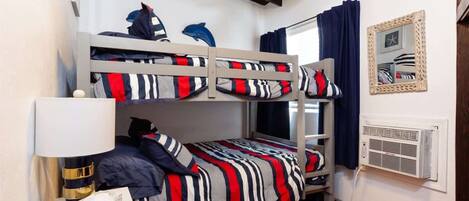 A bunk bed room with striped bedding, a bedside lamp, a mirror, and a window with curtains.