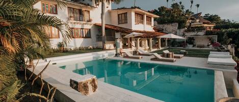 A pool with lounge chairs, a house with a balcony, and palm trees.