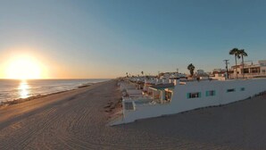 Un hotel frente al mar con vistas a la playa, edificios blancos y palmeras.