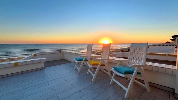 Una terraza con sillas blancas y vistas a la puesta de sol sobre el océano.