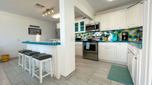 Una cocina con armarios blancos, microondas, estufa y una barra con taburetes.