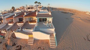 Una propiedad costera con varias edificaciones, una playa de arena y una escalera que lleva a una terraza.