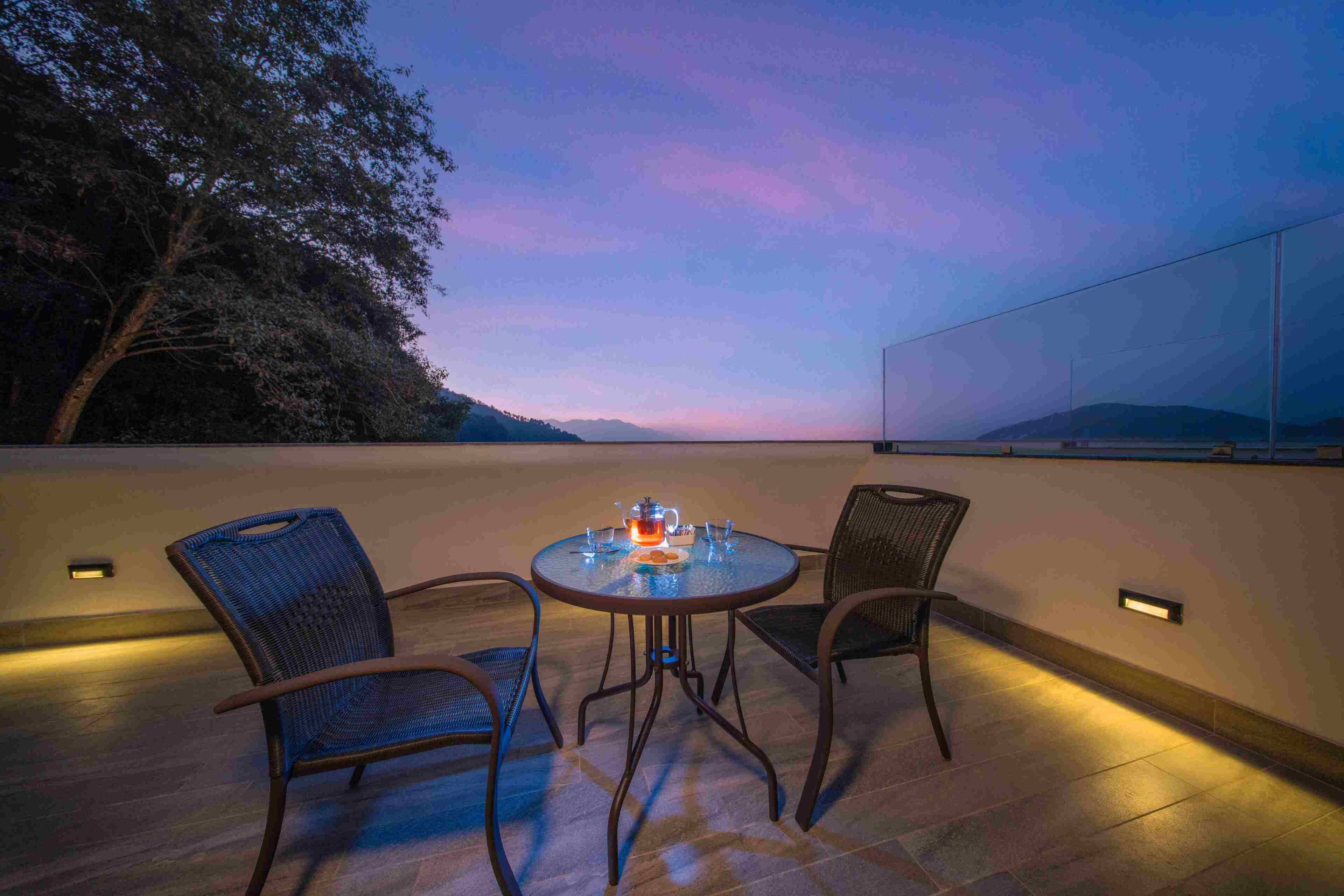 An outdoor dining area with a round table and two chairs, surrounded by a low wall and a view of the sky.