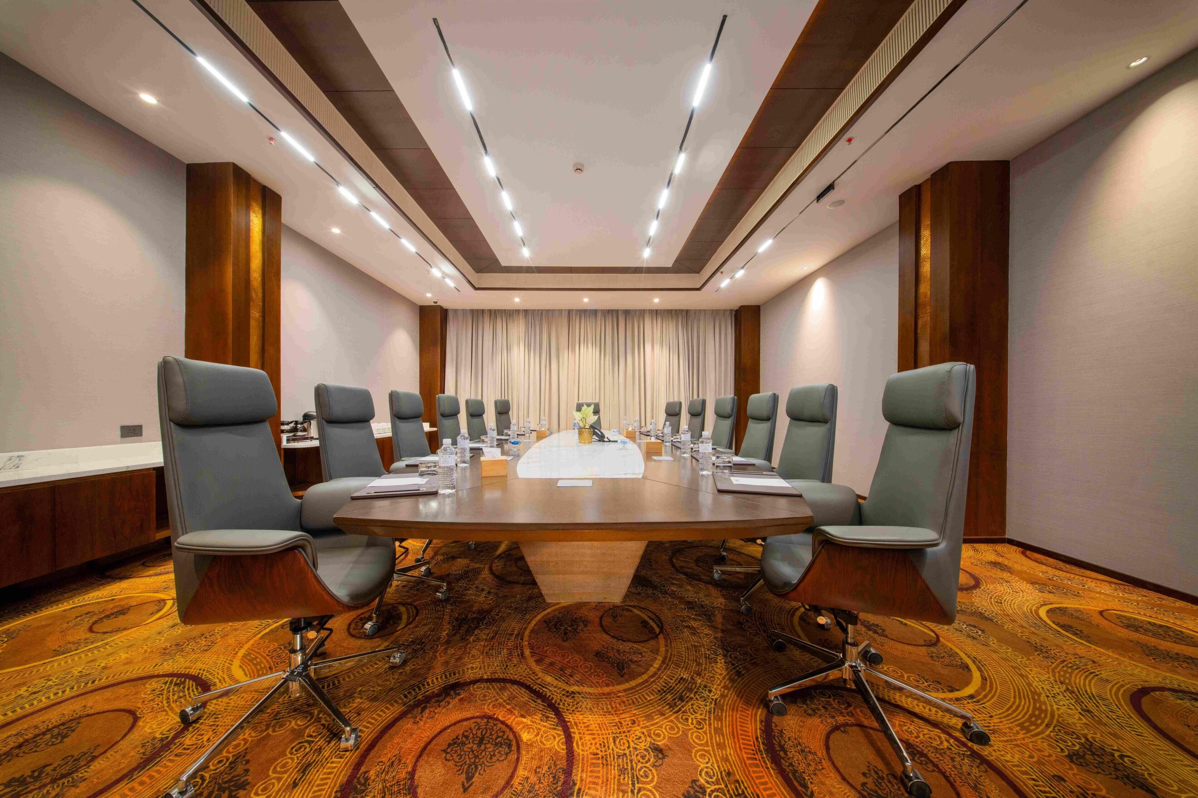 A conference room with a large oval table, eight chairs, a whiteboard, and a carpeted floor.