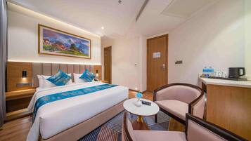 Una habitación de hotel con cama, escritorio, silla, un cuadro en la pared y una puerta.