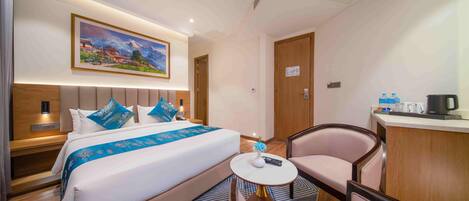A hotel room with a bed, a desk, a chair, a painting on the wall, and a door.