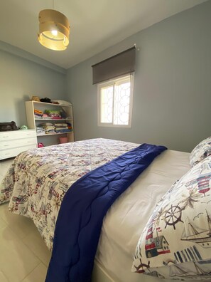 A bedroom with a bed, a wardrobe, a window, and a hanging light fixture.